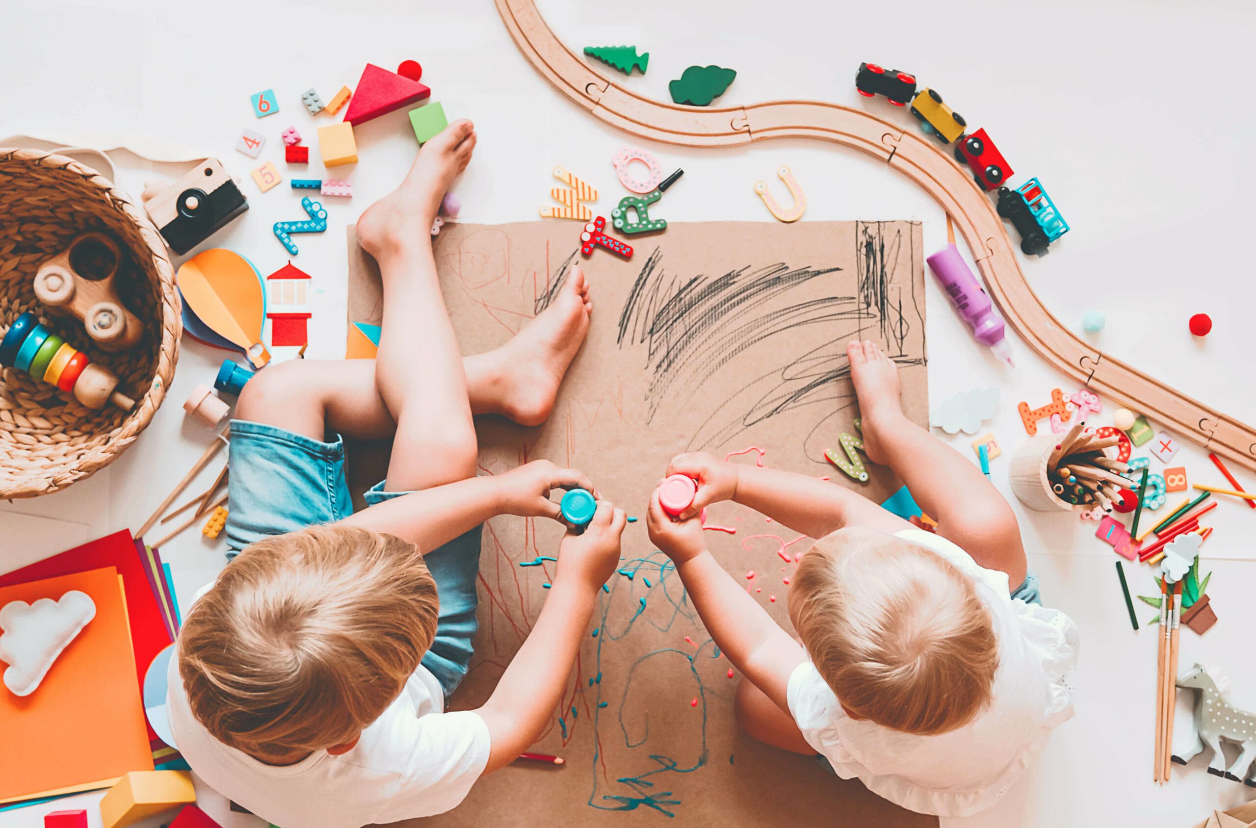 Dos niños pequeños pintando con colores sobre un cartón